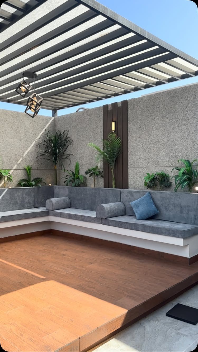 Modern outdoor patio with wooden decking, grey built-in seating, and a black metal pergola structure.