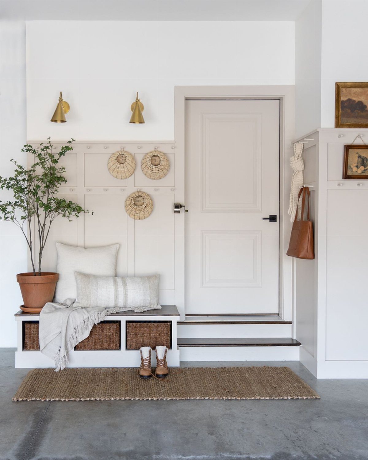 A white mudroom entryway with a built-in bench, wicker baskets, and a potted plant.