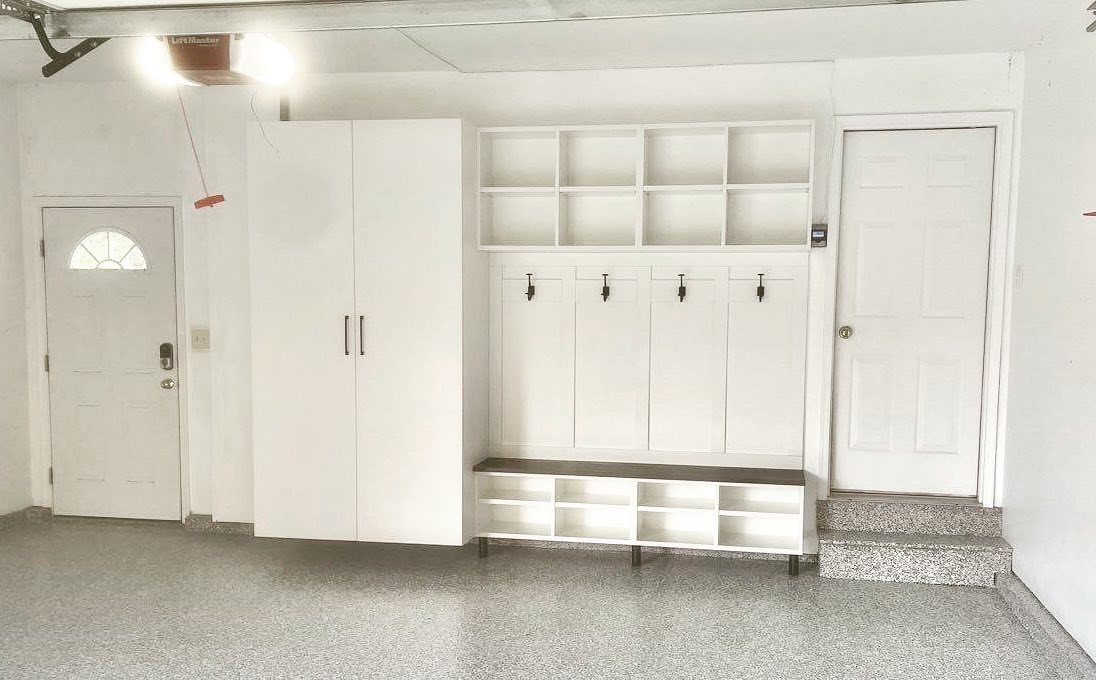 White mudroom storage unit with cubbies, hooks, and a bench installed in a garage.