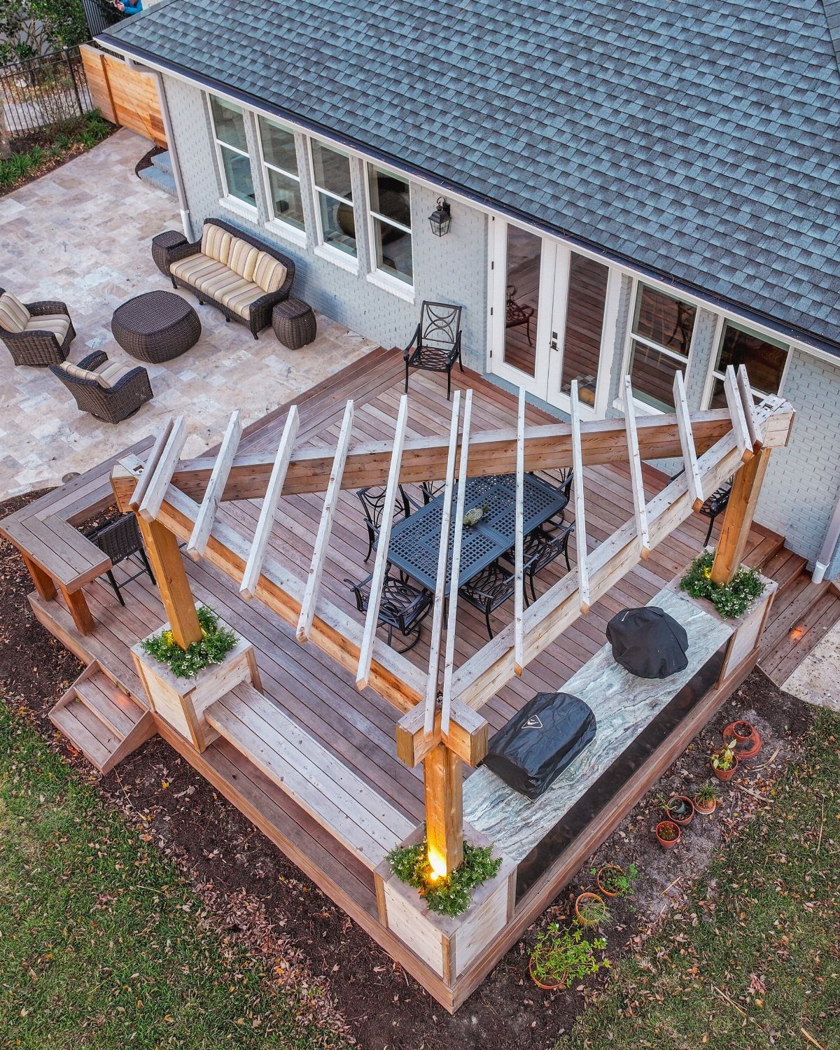 A multi-level wooden deck with a pergola and dining set overlooking a stone patio.