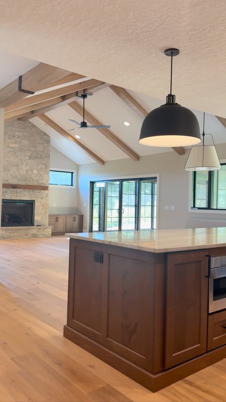 Exposed wooden beams stretch across a bright kitchen and living area with stone accents.