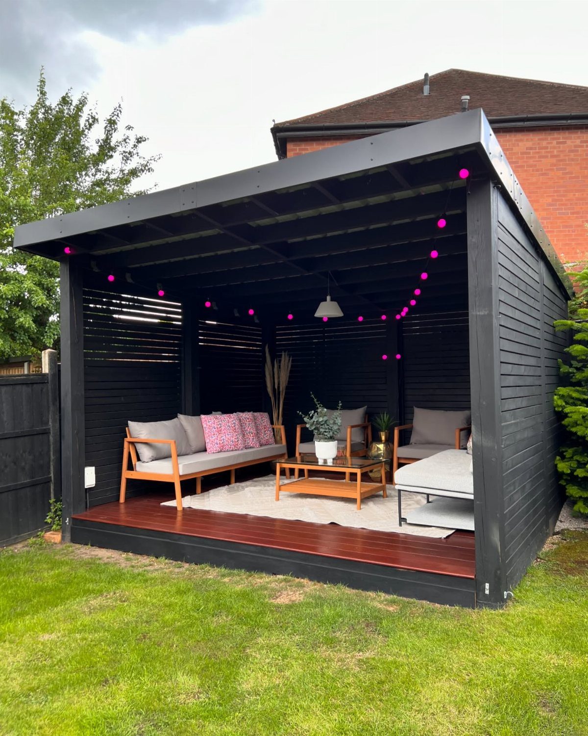 12 Deck with Gazebo Ideas for Outdoor Dining and Relaxation 2 A black wooden gazebo on a deck containing a sofa, coffee table, and a grey daybed.