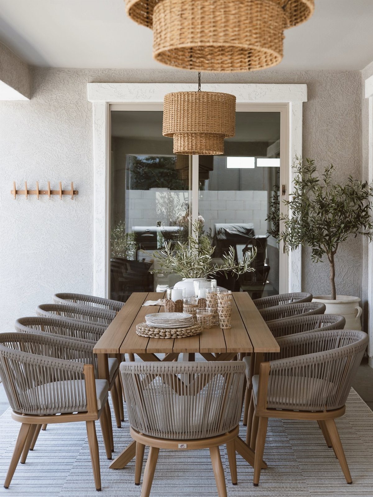 A wooden dining table with grey woven chairs set under large wicker pendant lights on a patio.