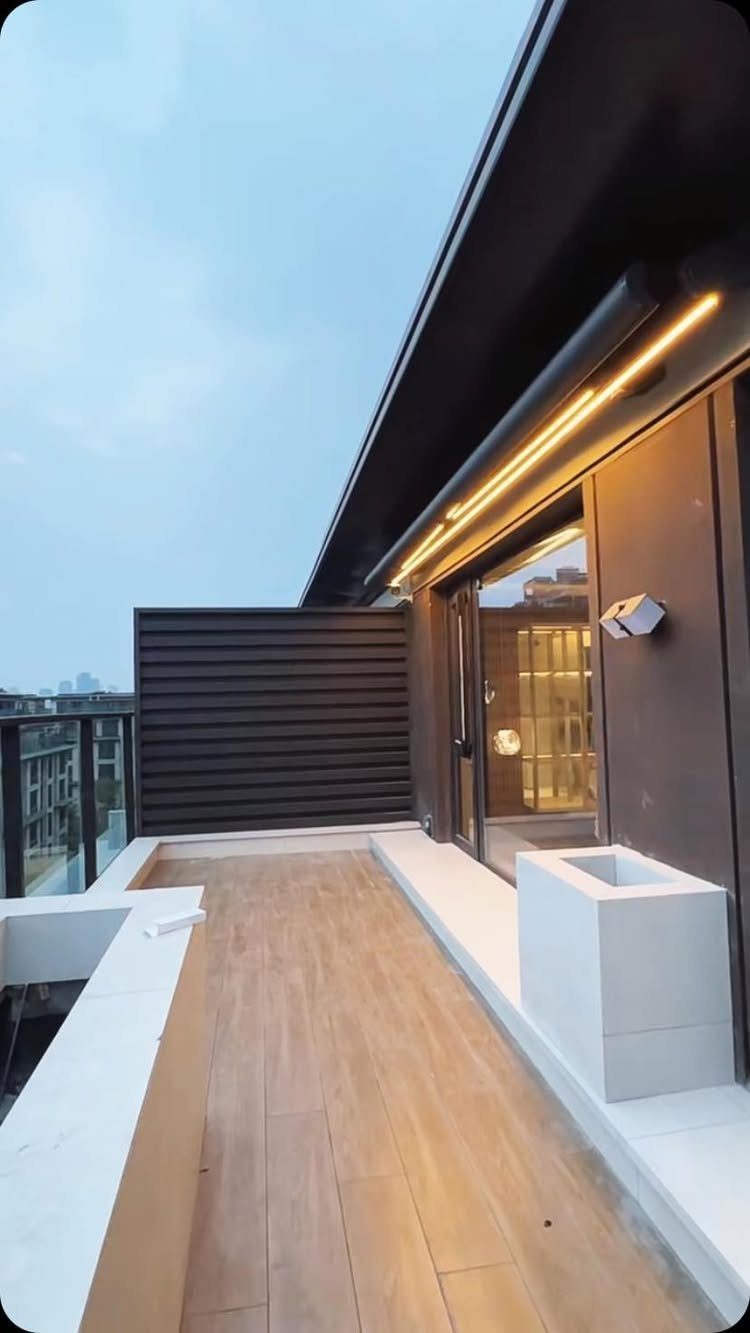 Modern balcony featuring a dark overhang with integrated LED strip lighting and wood-style flooring.