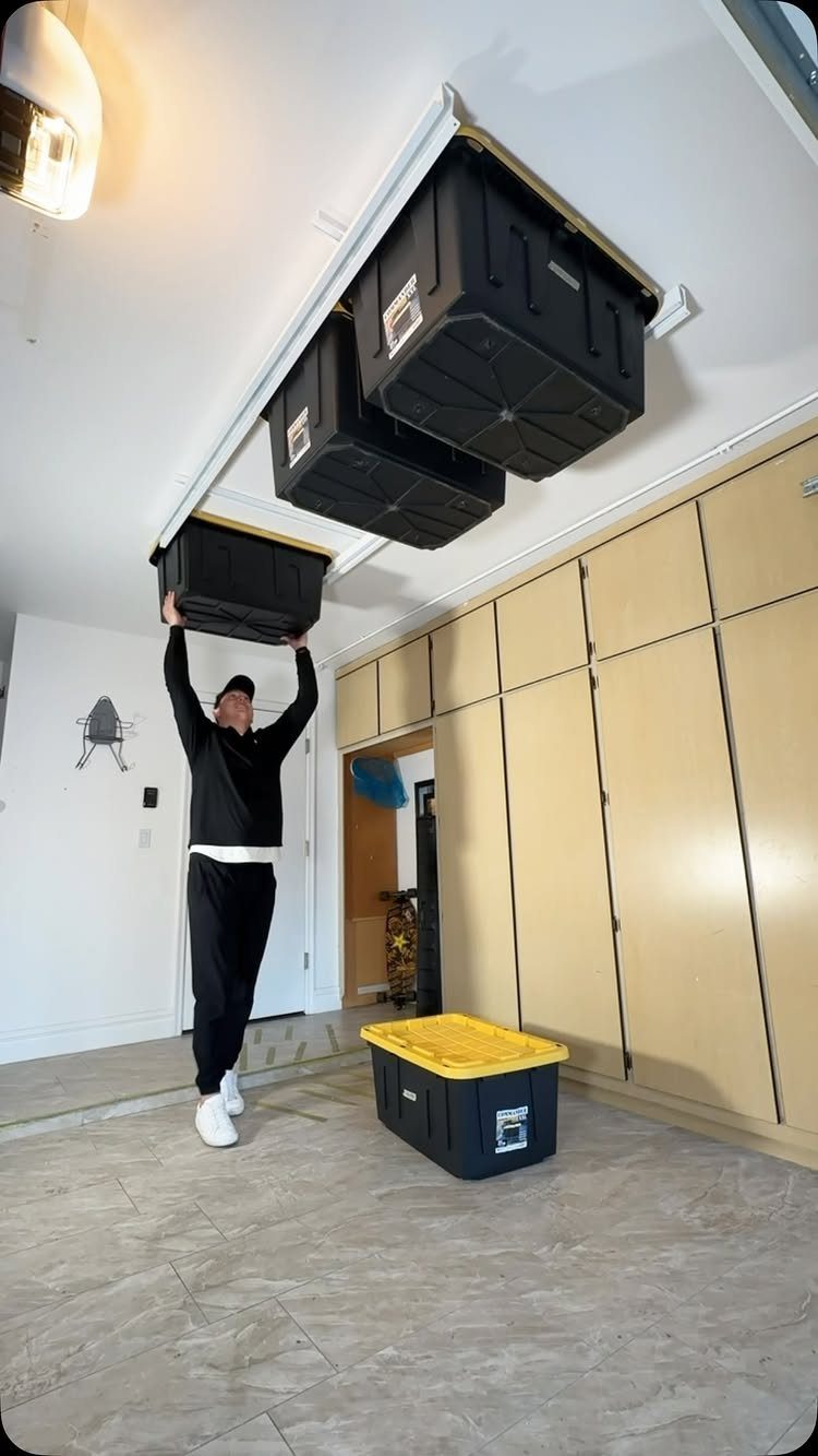 A man installing a black storage bin onto a white overhead ceiling rack system in a garage.