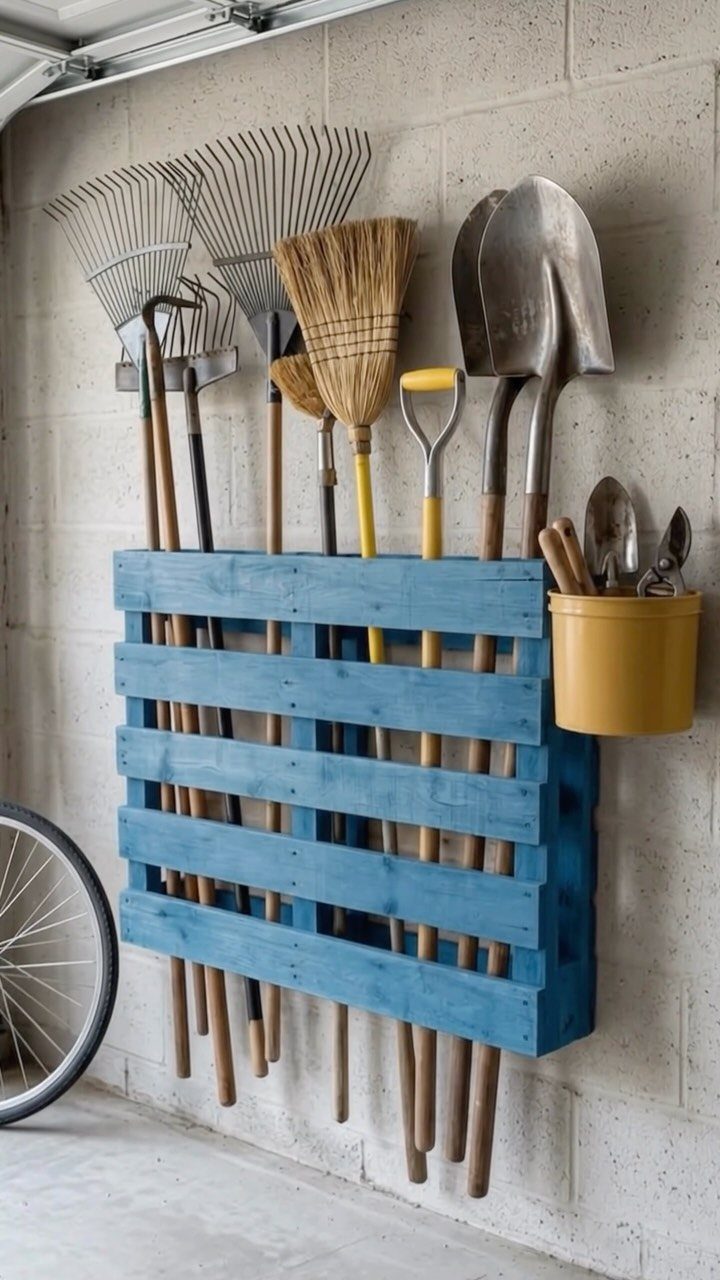 Garden tools like rakes and shovels stored in a blue wooden pallet rack on a garage wall.