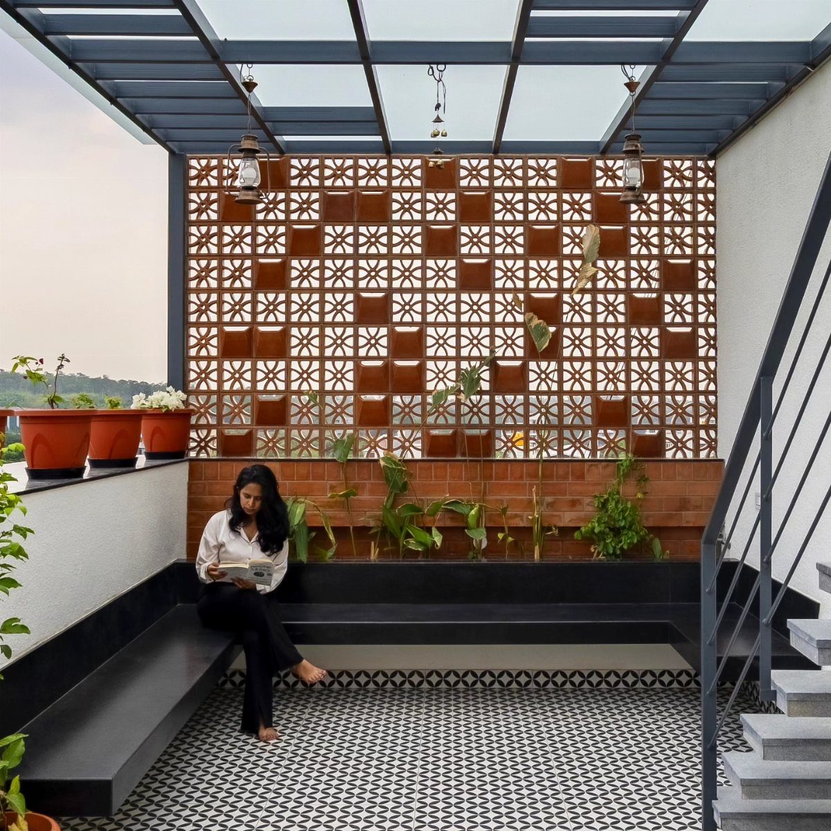 A woman sits on a built-in patio bench under a modern metal pergola structure.