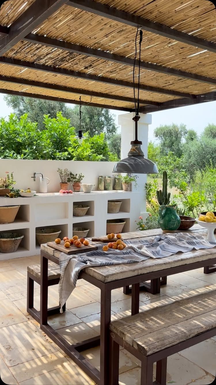 10 Wooden Garden Kitchen Ideas for Warm Outdoor Cooking 2 Wooden dining table and benches under a reed pergola with a white outdoor kitchen in the background.