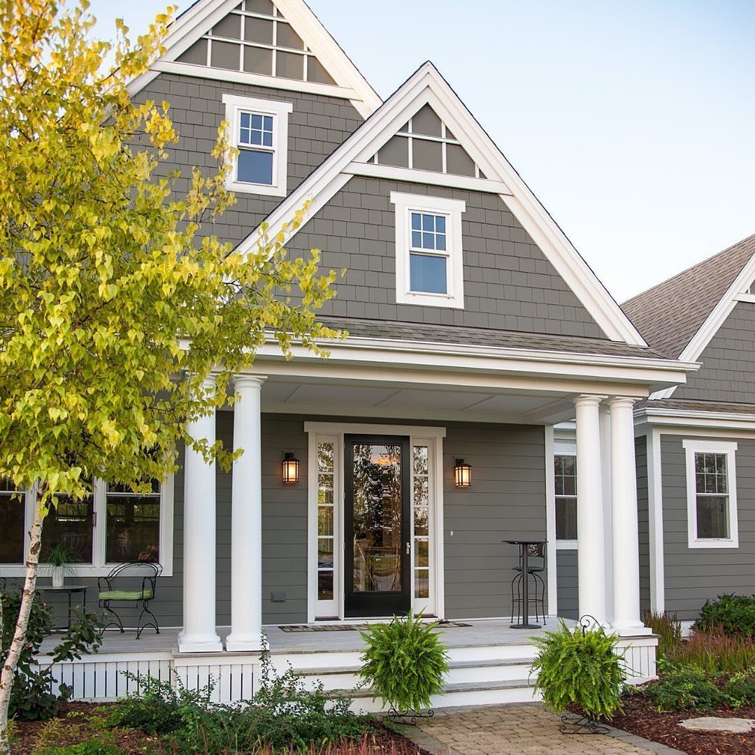 12 Trending House Colors for Exterior Looks in 2026 2 A gray shingle house with white trim, columns, and a front porch under a clear sky.