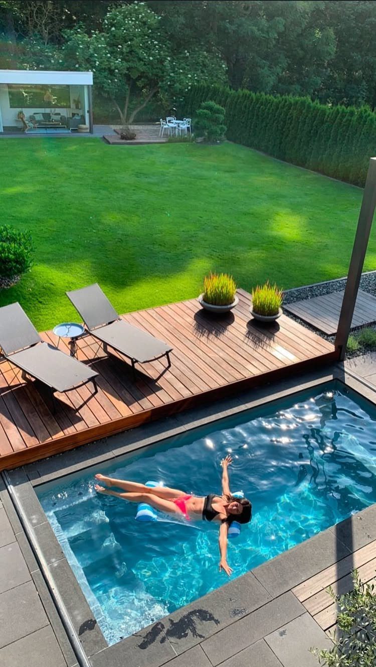 Wooden deck with lounge chairs situated next to a bright blue swimming pool in a backyard.