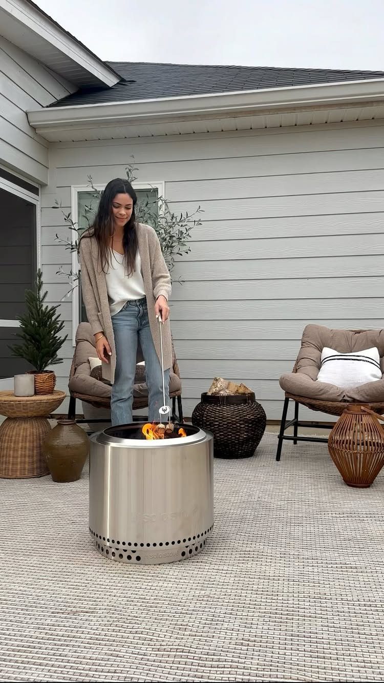 A woman tending a small stainless steel portable fire pit on a patio.