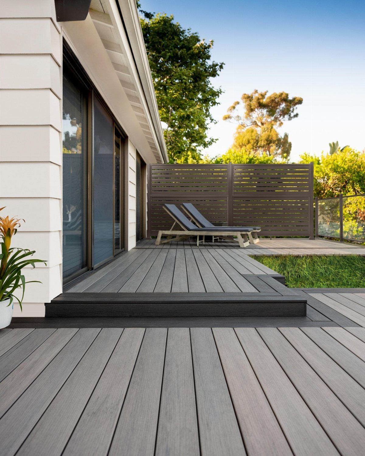 14 Deck Balustrade Ideas for Every Style, from Glass to Stone 8 Grey composite deck with a dark horizontal slat privacy screen railing and lounge chairs.