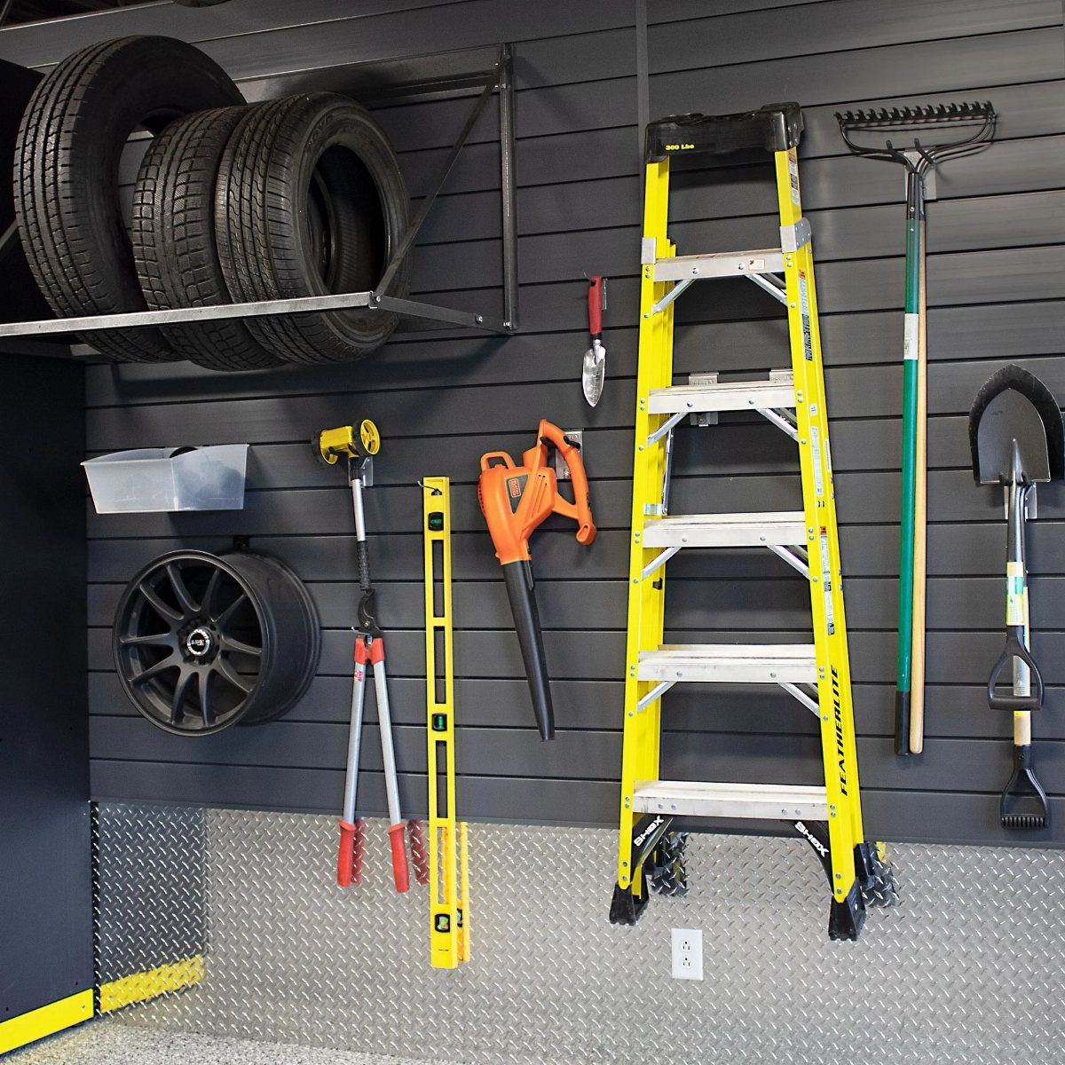 9 Shed Yard Tool Storage Ideas for Every Wall and Corner 5 Various garage tools and tires hanging on a dark grey PVC slatwall storage system.