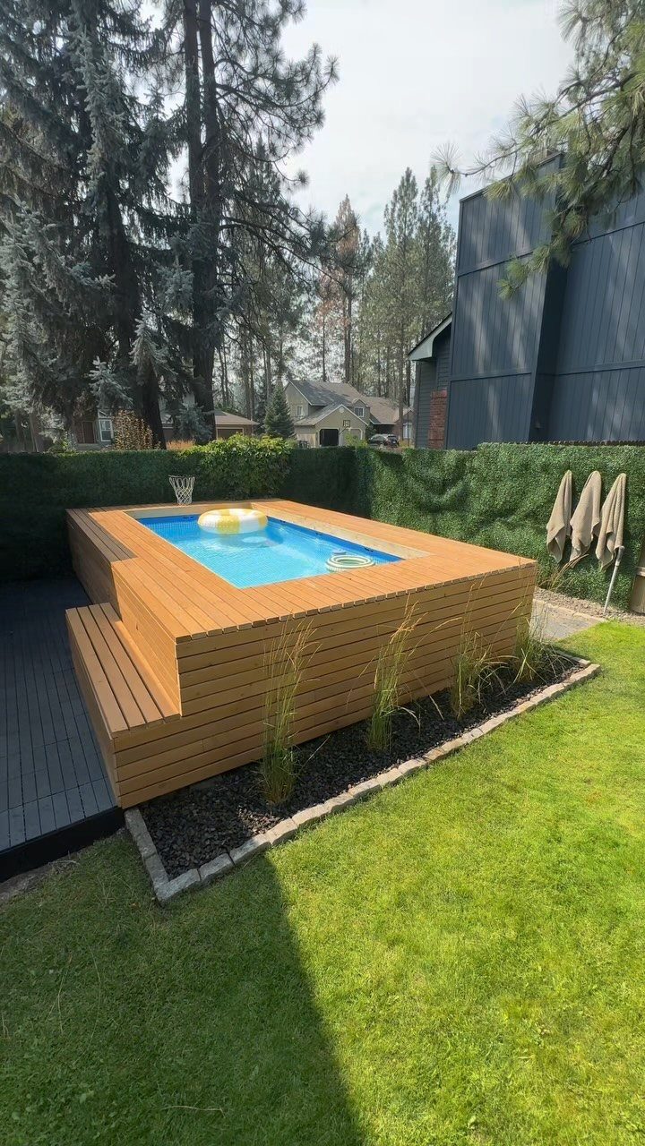 A light brown wooden deck built around a small rectangular blue swimming pool outdoors.