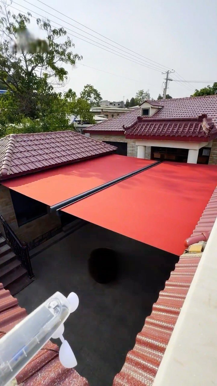 A bright red retractable awning extended over a dark outdoor patio area next to a tiled roof.