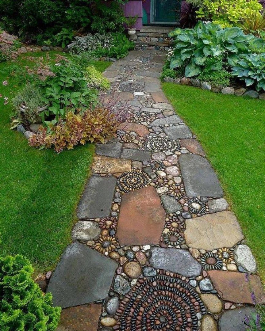 A decorative stone pathway with pebble mosaic patterns winding through a lush green garden lawn.