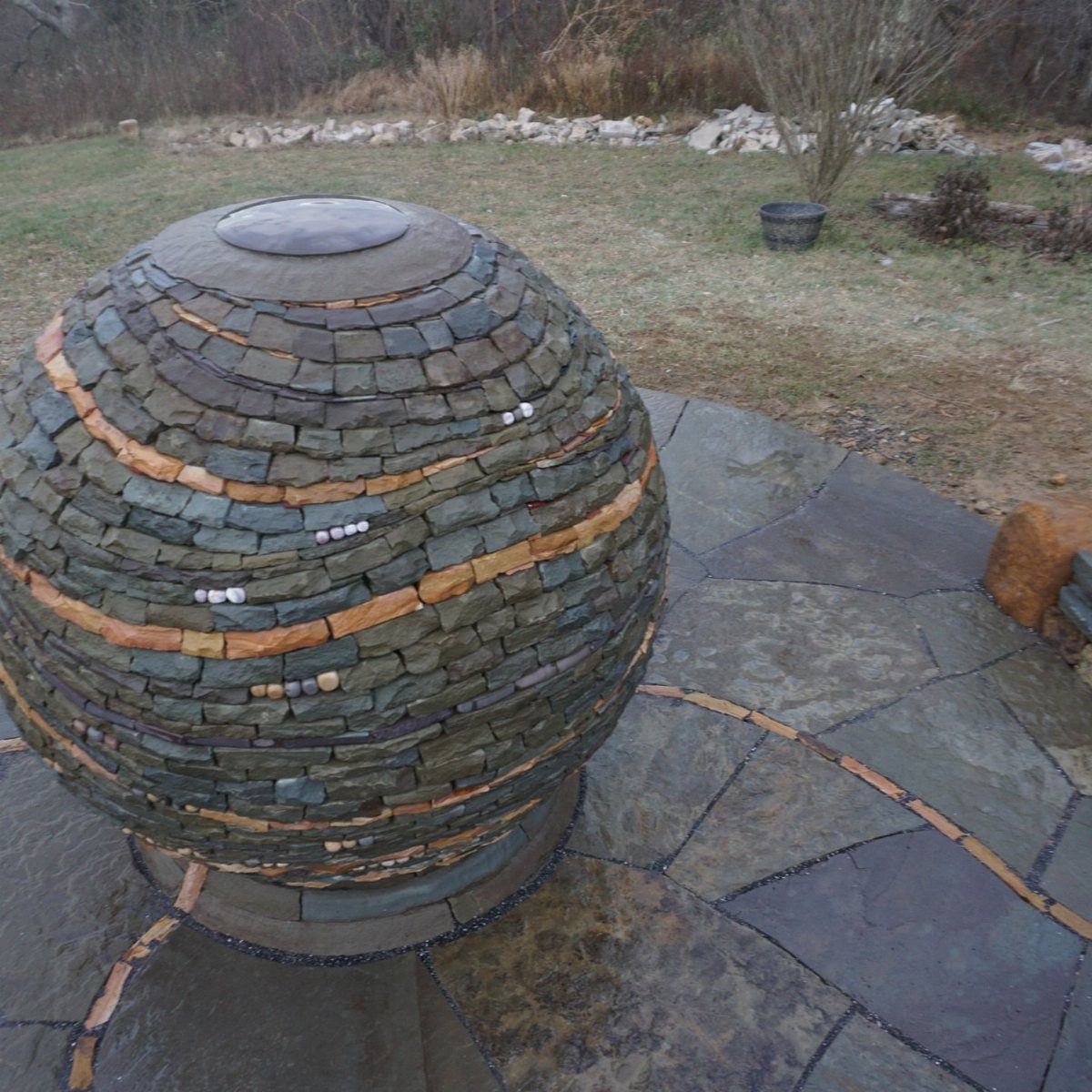 A large spherical sculpture made of stacked flat stones sitting on a stone patio.