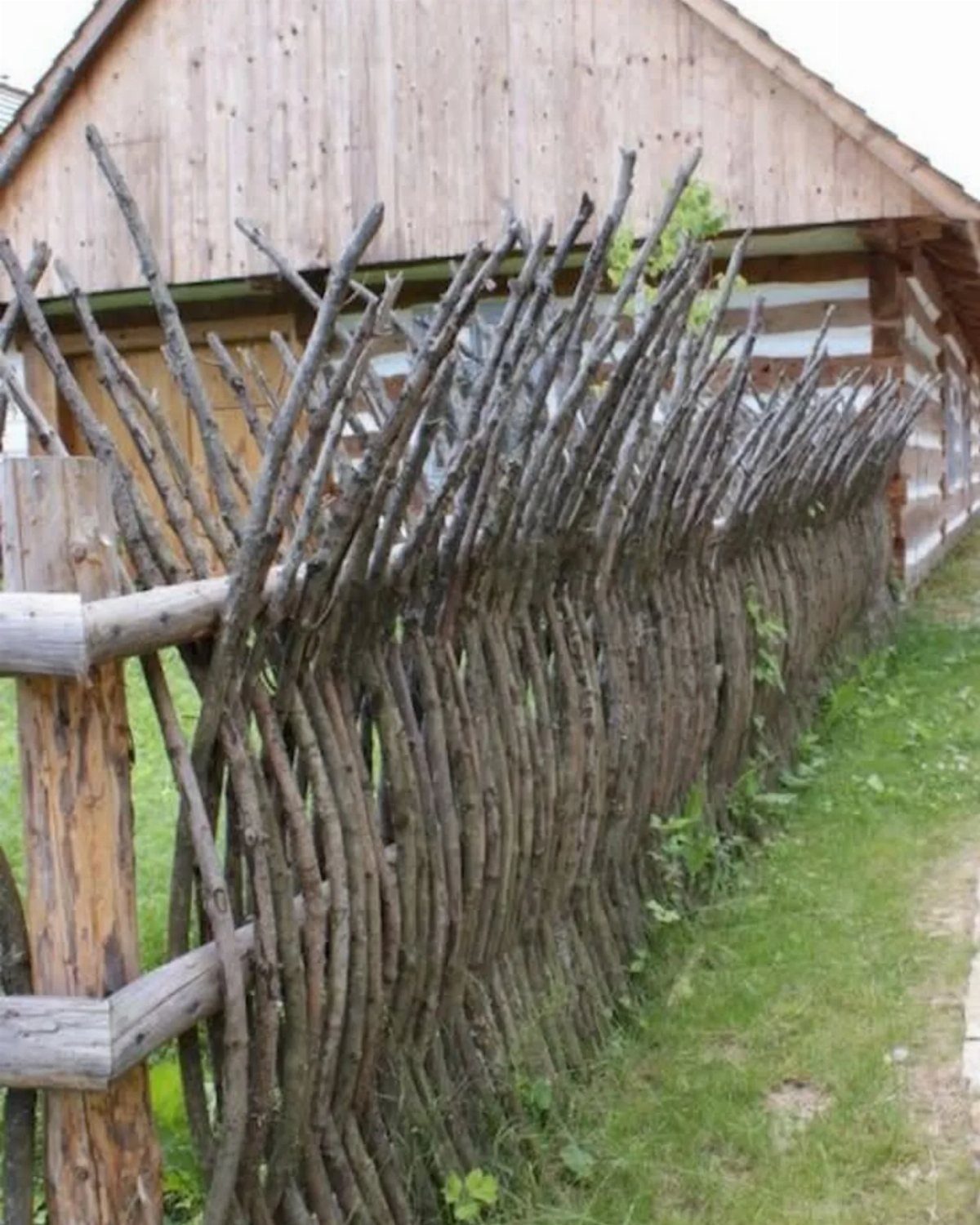 A rustic wooden fence made of woven branches in front of a wooden building.
