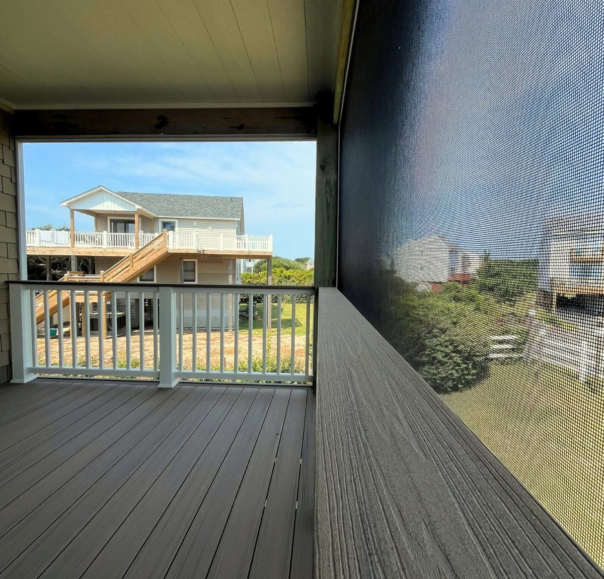 17 Beach House Deck Ideas for Oceanfront Living 9 A grey composite deck viewed through a large black insect screen overlooking a coastal house.
