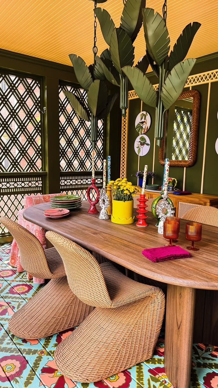 A wooden dining table with wicker chairs set inside a colorful screened-in porch.