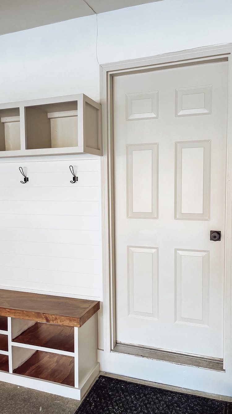 White shiplap walls and a wooden bench sit next to a white paneled door.