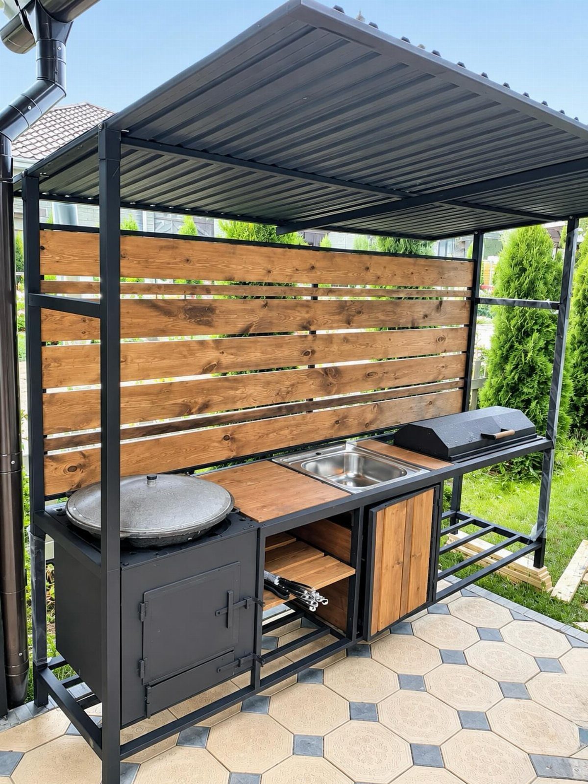 10 Wooden Garden Kitchen Ideas for Warm Outdoor Cooking 5 A small outdoor kitchen with a black metal frame, wood backsplash, grill, and sink.