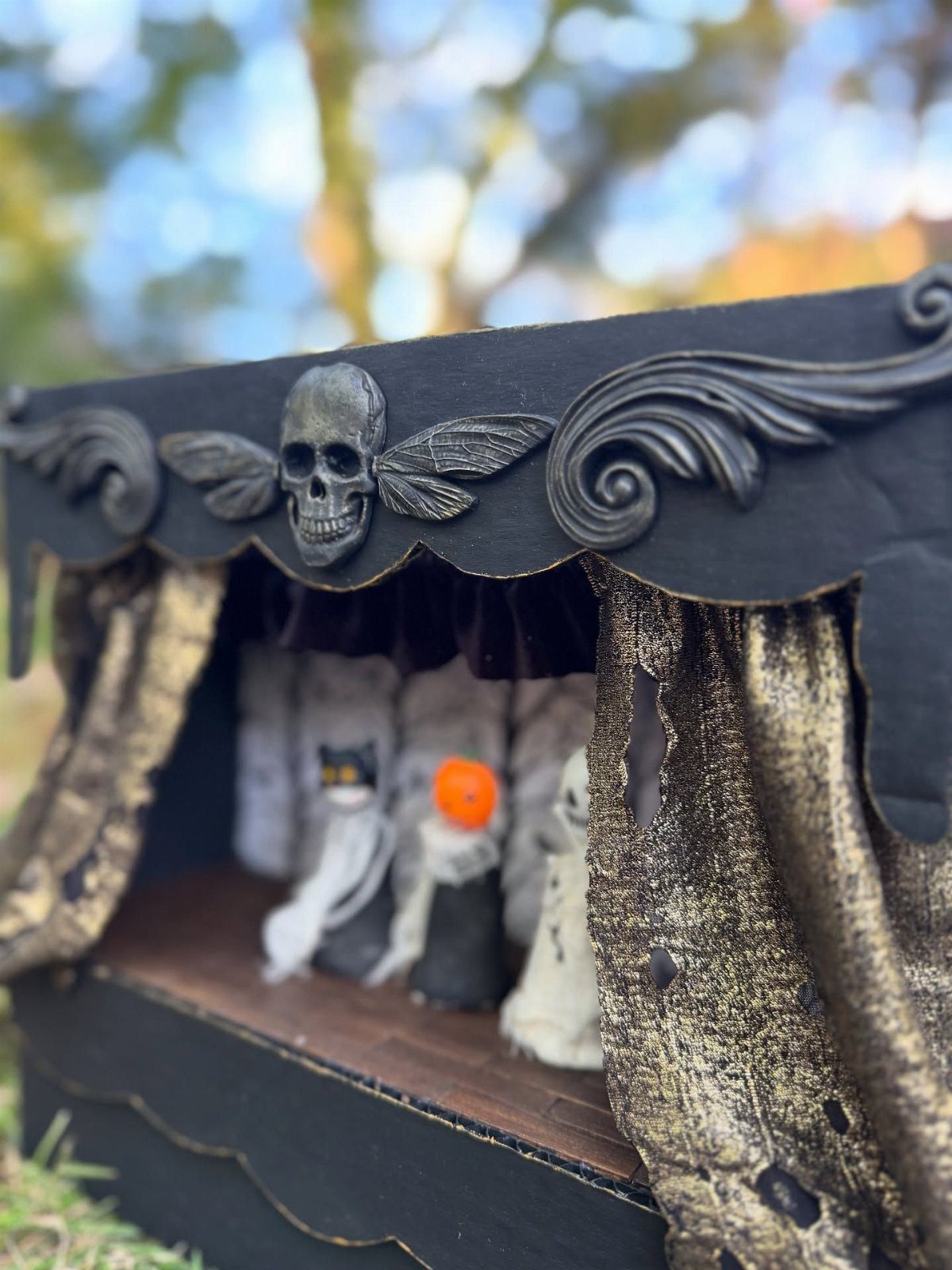A miniature black and gold spooky puppet theater featuring small white ghost puppets inside.