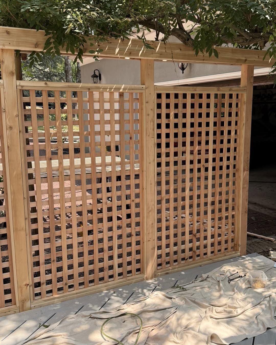 A light-colored wooden lattice fence structure stands under the shade of green leafy trees.
