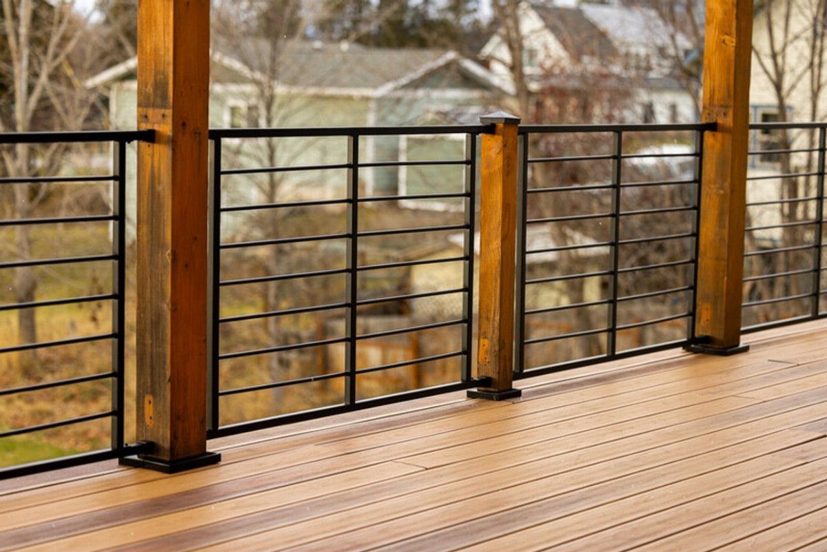 Black metal railing with horizontal cables installed on a wooden deck overlooking a neighborhood.