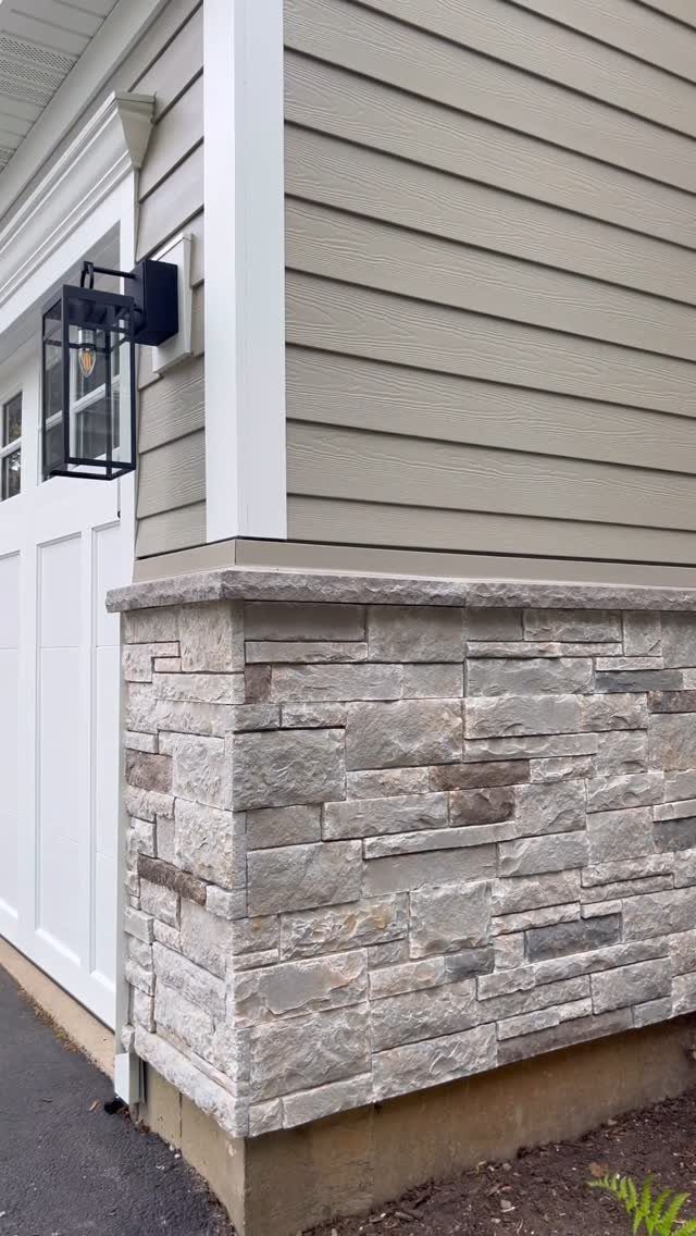 A house exterior showing tan horizontal siding above a grey and beige stone veneer foundation.