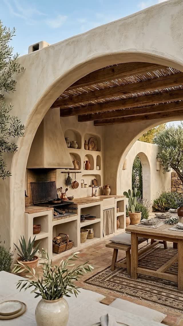 Built-in stucco outdoor kitchen under a wooden pergola with a dining table nearby.