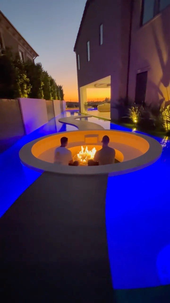 Two people sitting inside a circular sunken fire pit surrounded by glowing blue pool water.