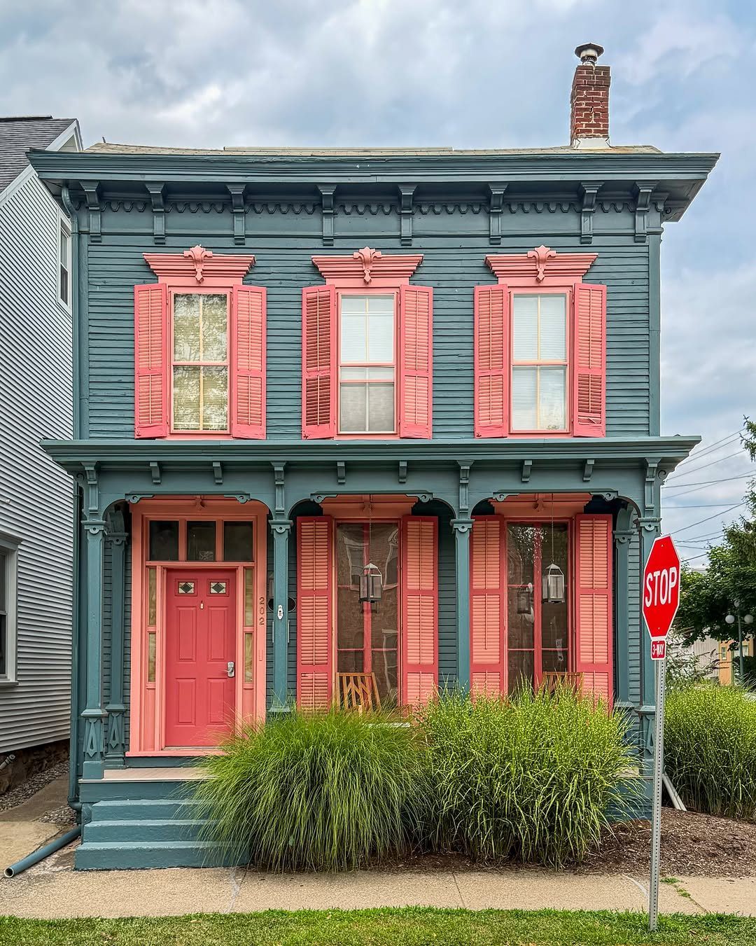 A blue-grey Victorian house with salmon-pink shutters, trim, and a matching front door.
