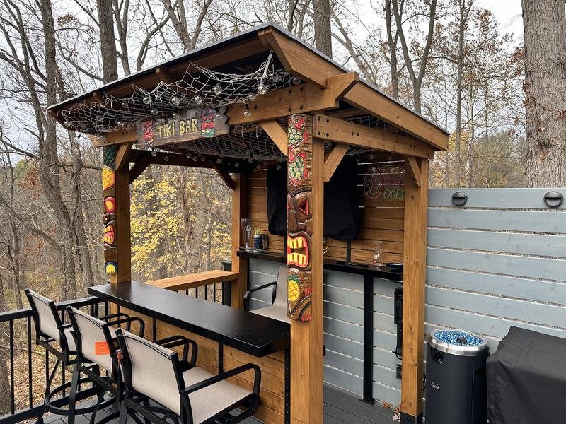 A wooden tiki bar structure with tiki carvings and a black countertop on a deck.
