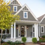 A gray shingle house with white trim, columns, and a front porch under a clear sky.