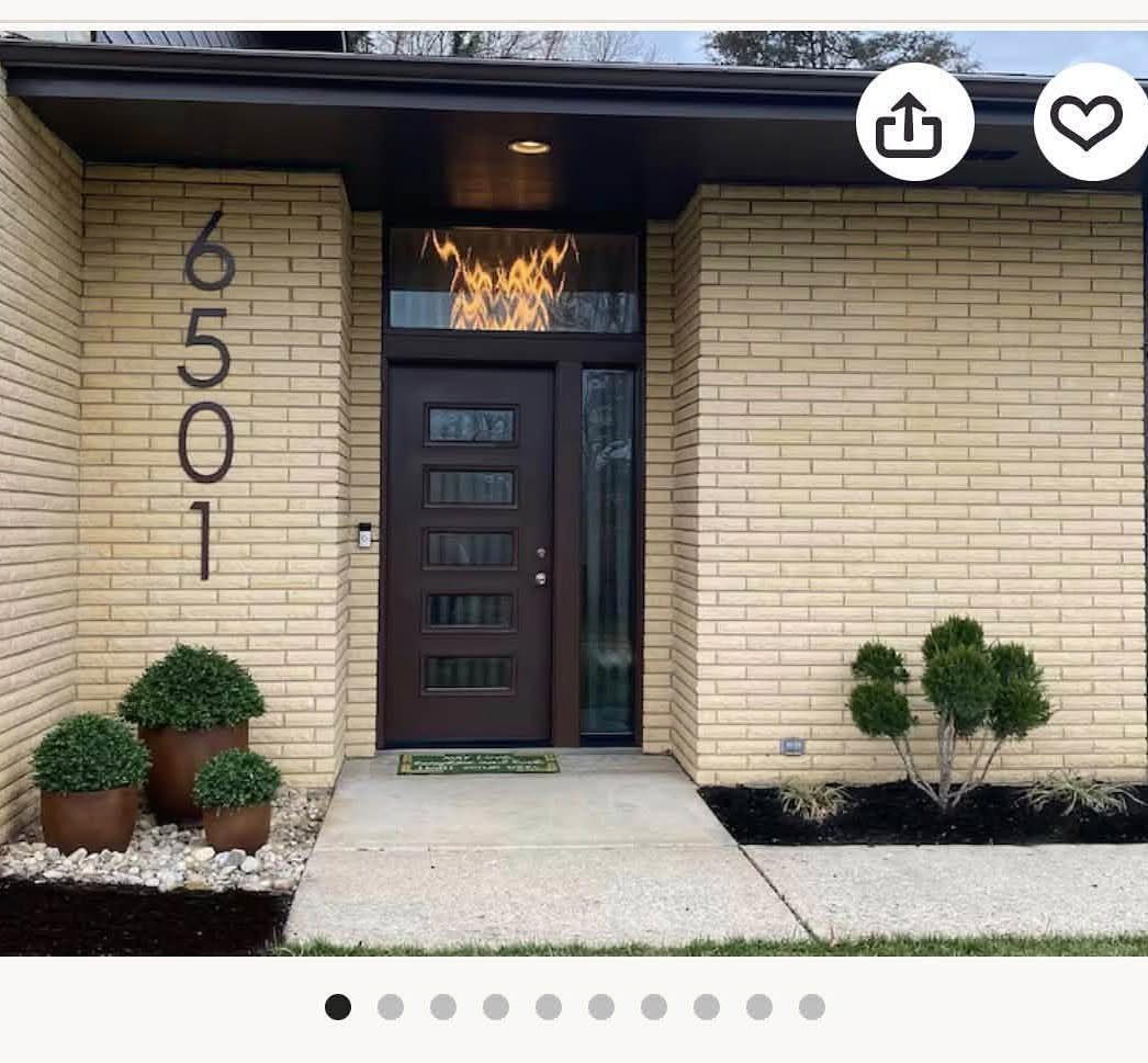 Modern dark vertical house numbers mounted on a light tan brick exterior wall next to a door.