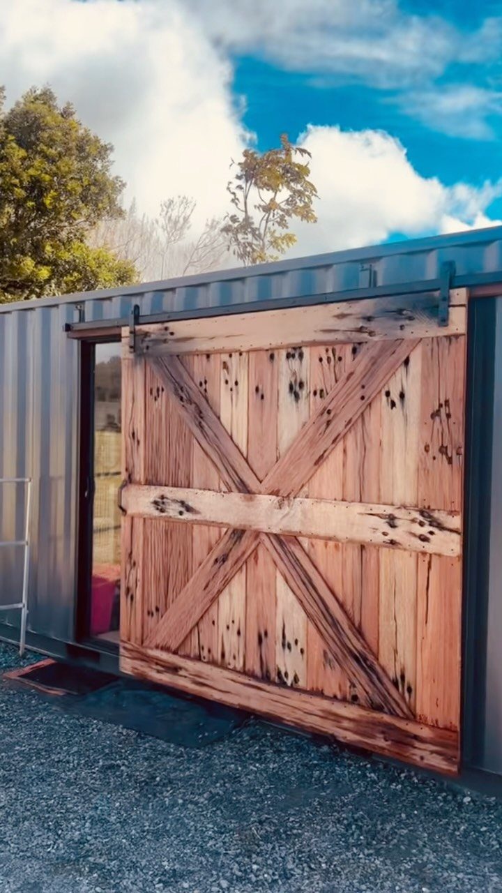 A large rustic wooden sliding barn door mounted on a dark metal container structure.