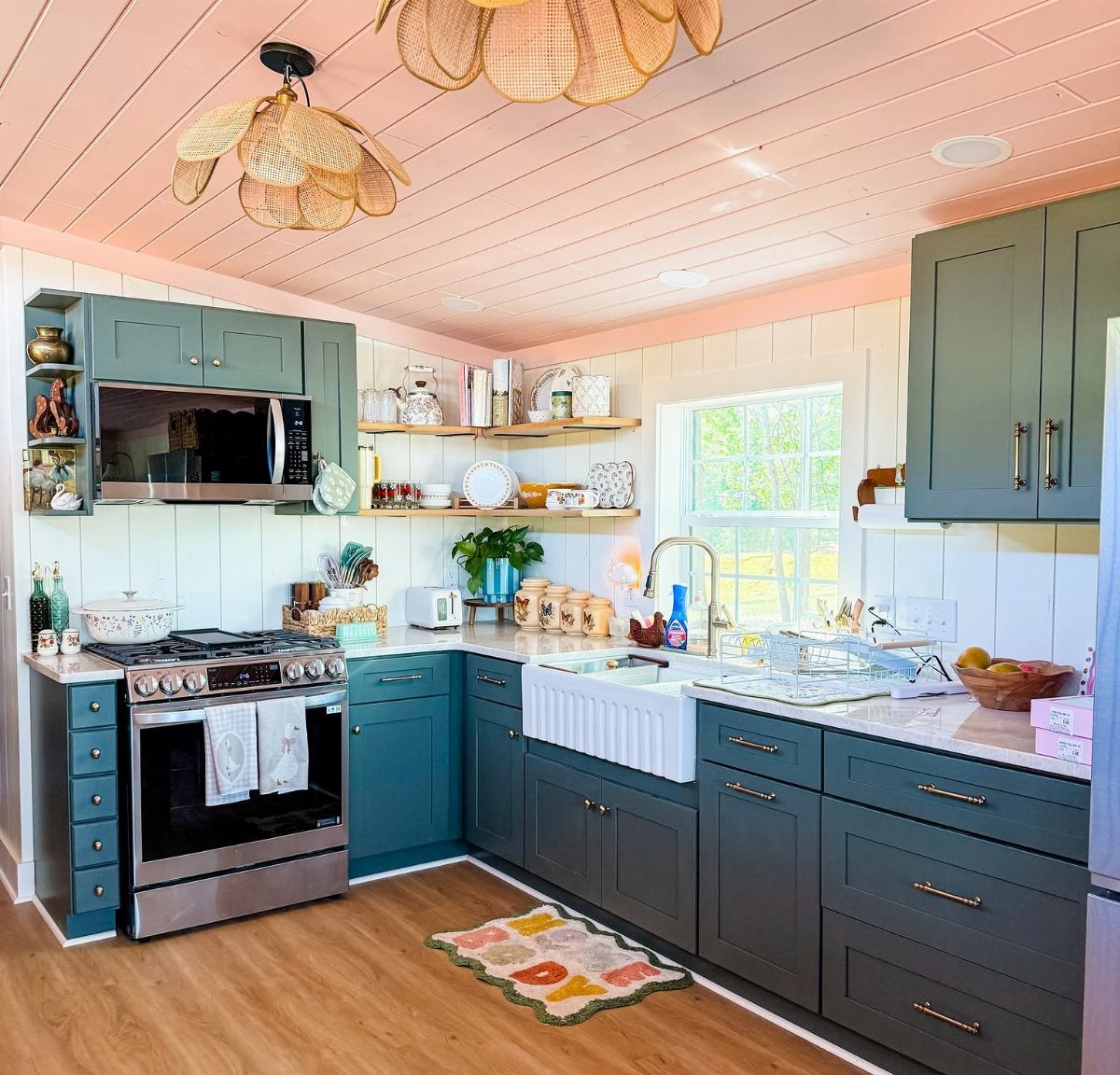 A bright kitchen with teal cabinets, white paneled walls, and a pink wood ceiling.