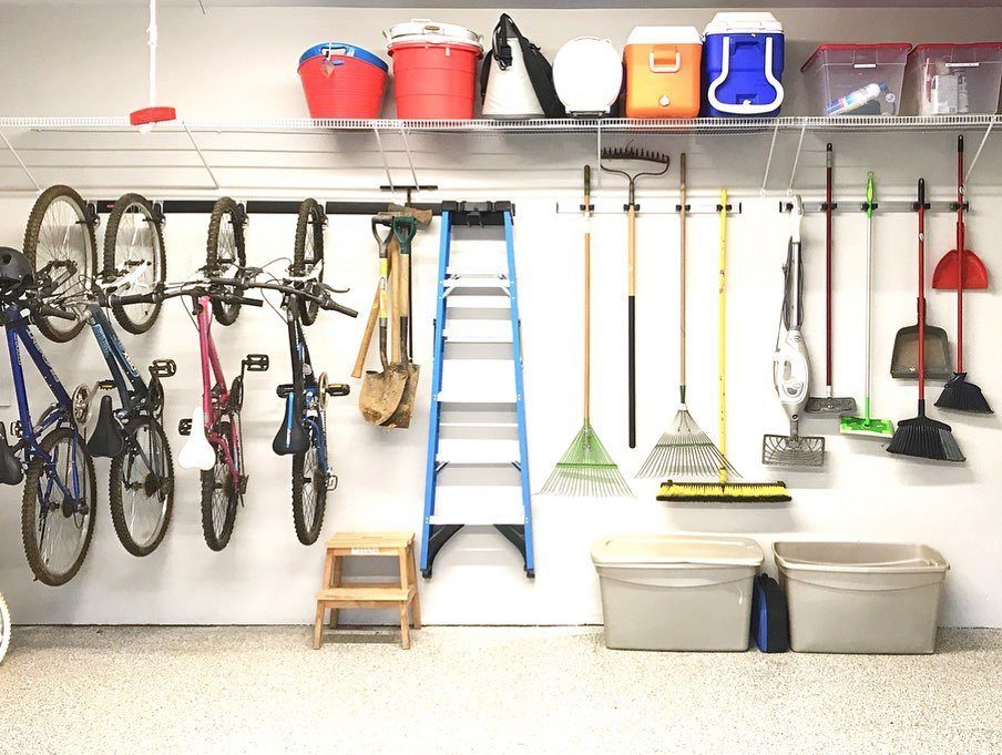 Bicycles, a ladder, and various garden tools hanging organized on a white garage wall.
