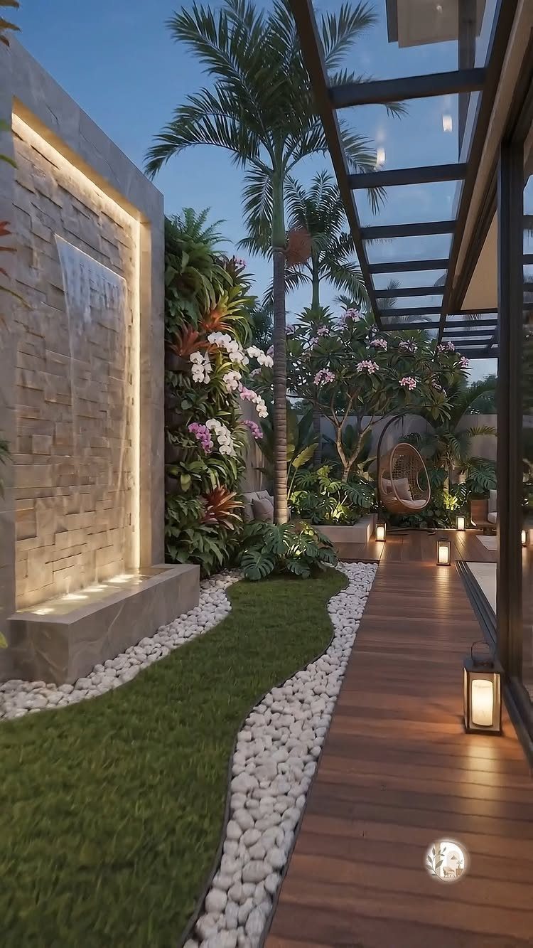A modern patio with a stone water feature, tropical plants, and a wooden deck walkway.