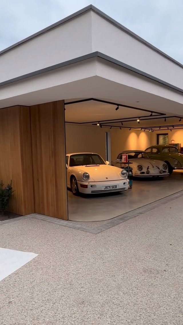 A modern white detached garage with open wooden doors revealing vintage cars parked inside.