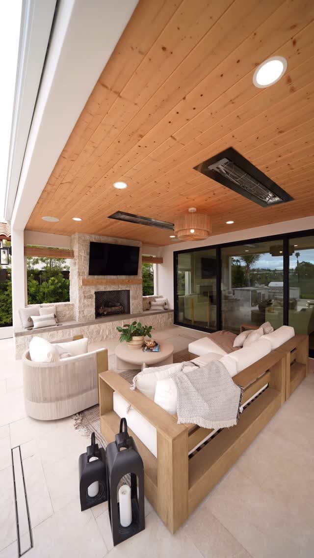A modern outdoor patio with a wood plank ceiling, stone fireplace, and comfortable lounge seating.