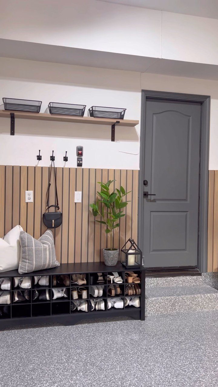 A modern mudroom entryway with a grey door, slat wall, shoe bench, and storage baskets.